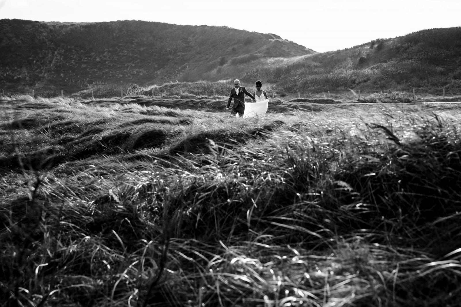 Bruidspaar loopt samen door de winderige duinen tijdens hun trouwshoot.