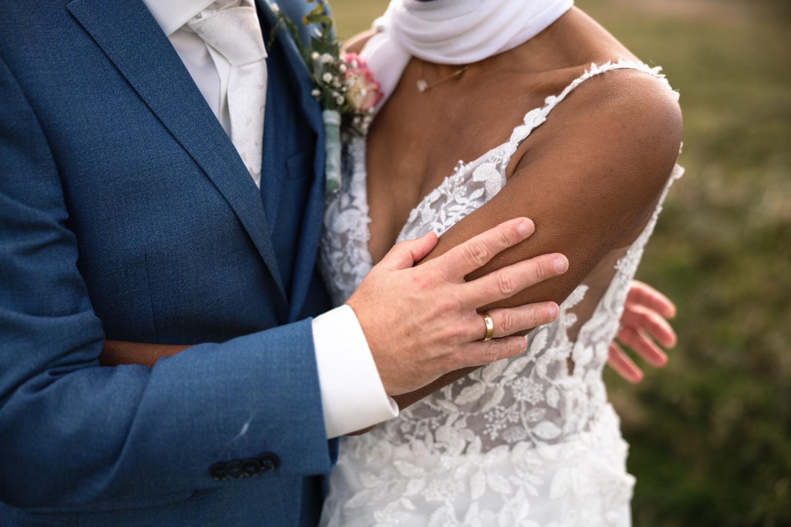Close-up van de bruidegom die de koude bruid met kippenvel liefdevol omhelst op haar op te warmen tijdens de fotoshoot.