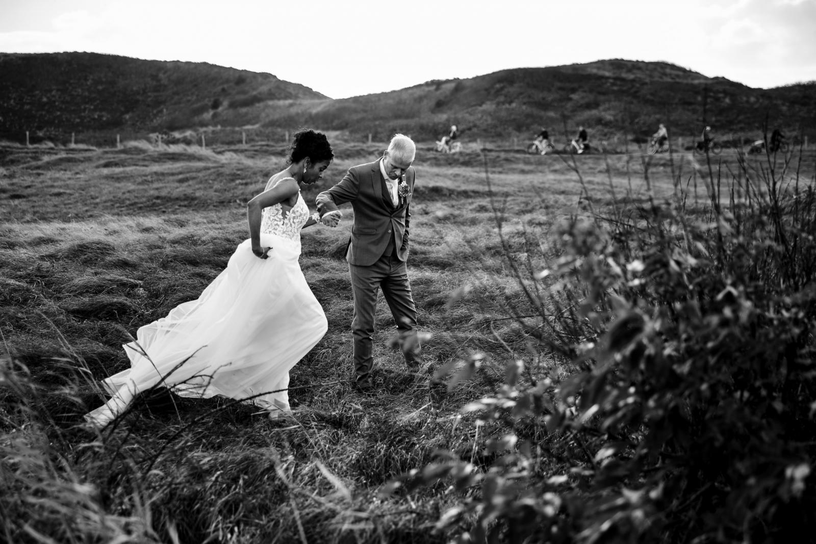Bruidspaar wandelt hand in hand door de duinen op hun trouwdag.