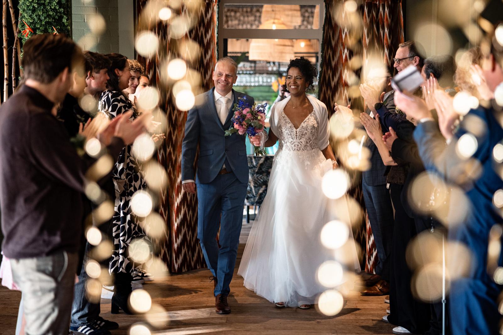 Bruidspaar Farida en Hans maakt feestelijke entree bij Strandpaviljoen STRUI terwijl gasten applaudisseren.