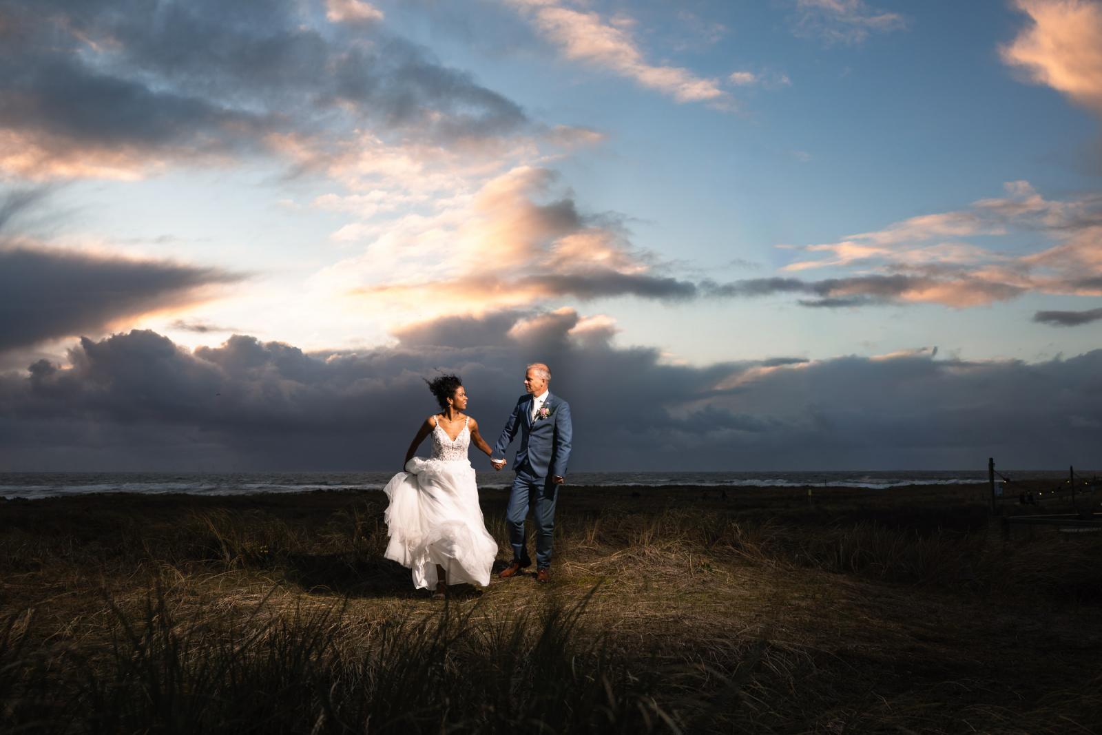 Farida en Hans rennen lachend door de duinen tijdens een dramatische zonsondergang bij Camperduin.