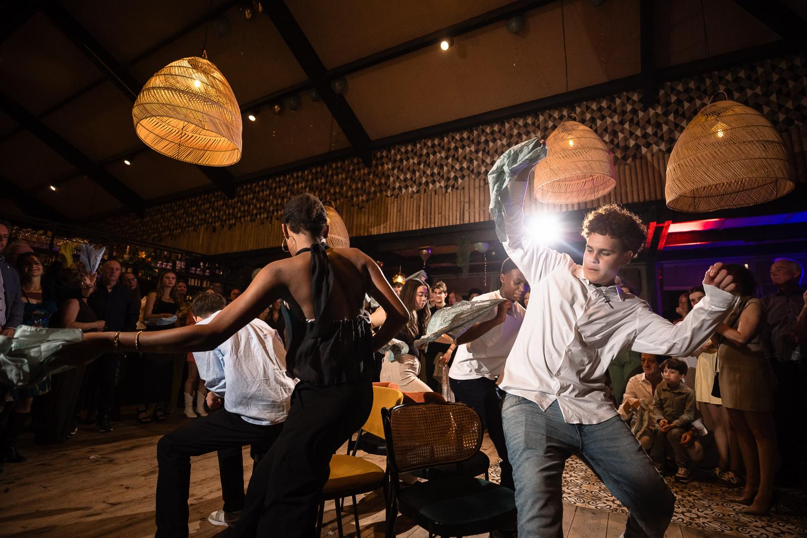 Grote groep feestende gasten die synchroon dansen en hurken tijdens het trouwfeest met kleurrijke verlichting.