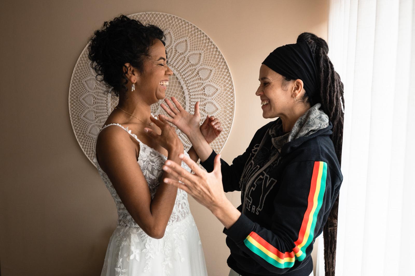 Bruid Farida lacht samen met haar zus vlak voor het aantrekken van haar trouwjurk, een ontspannen en vrolijk moment in het ochtendlicht.