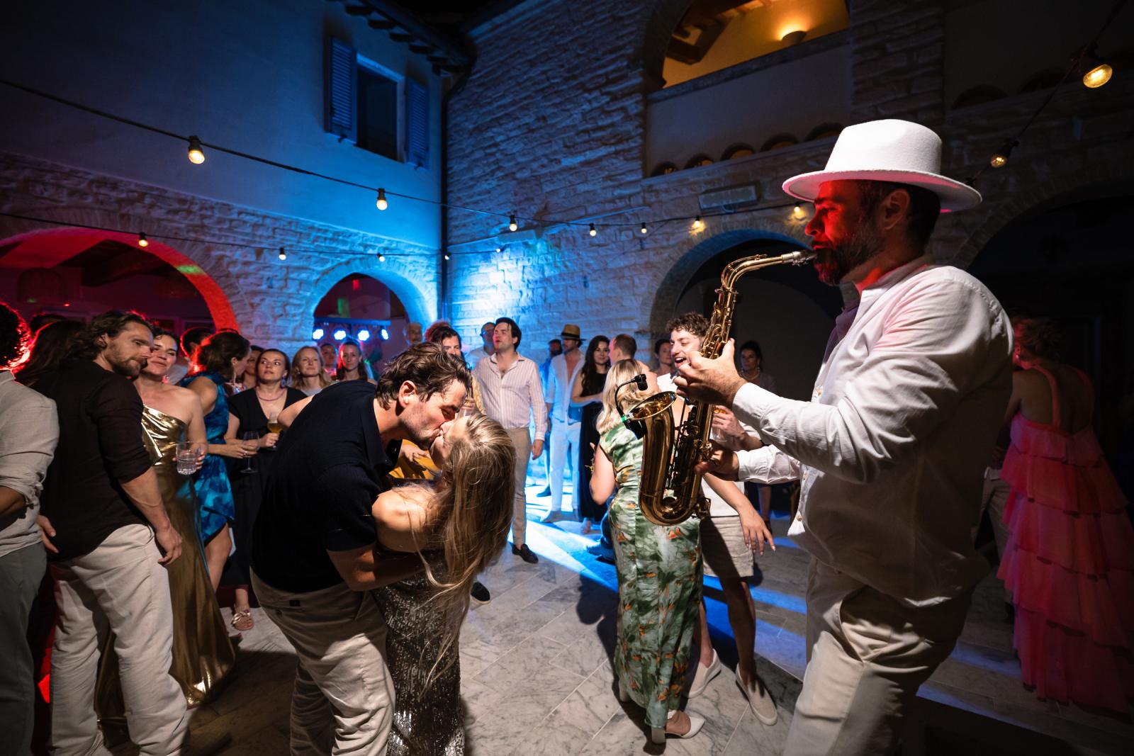 Groom Niels kissing bride Gemmy on courtyard dance floor while saxophonist performs beside them