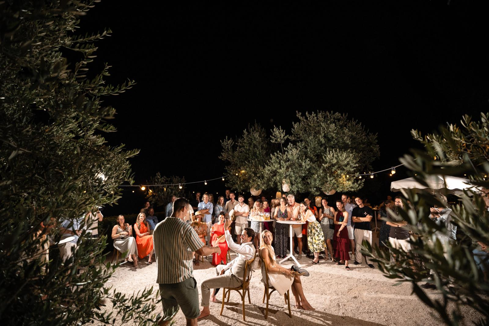 Bride and groom playing the shoe game during evening reception surrounded by guests at Le Stonghe