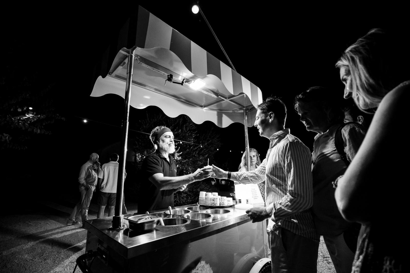 Black and white photo of wedding guests getting fresh Italian gelato from a vintage cart at night