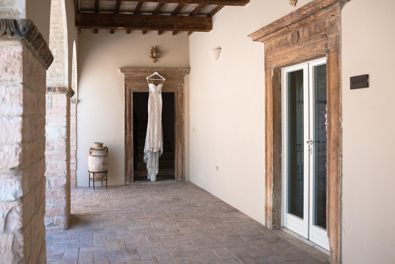 Bridal gown hanging in a rustic stone archway of Le Stonghe venue before the wedding ceremony