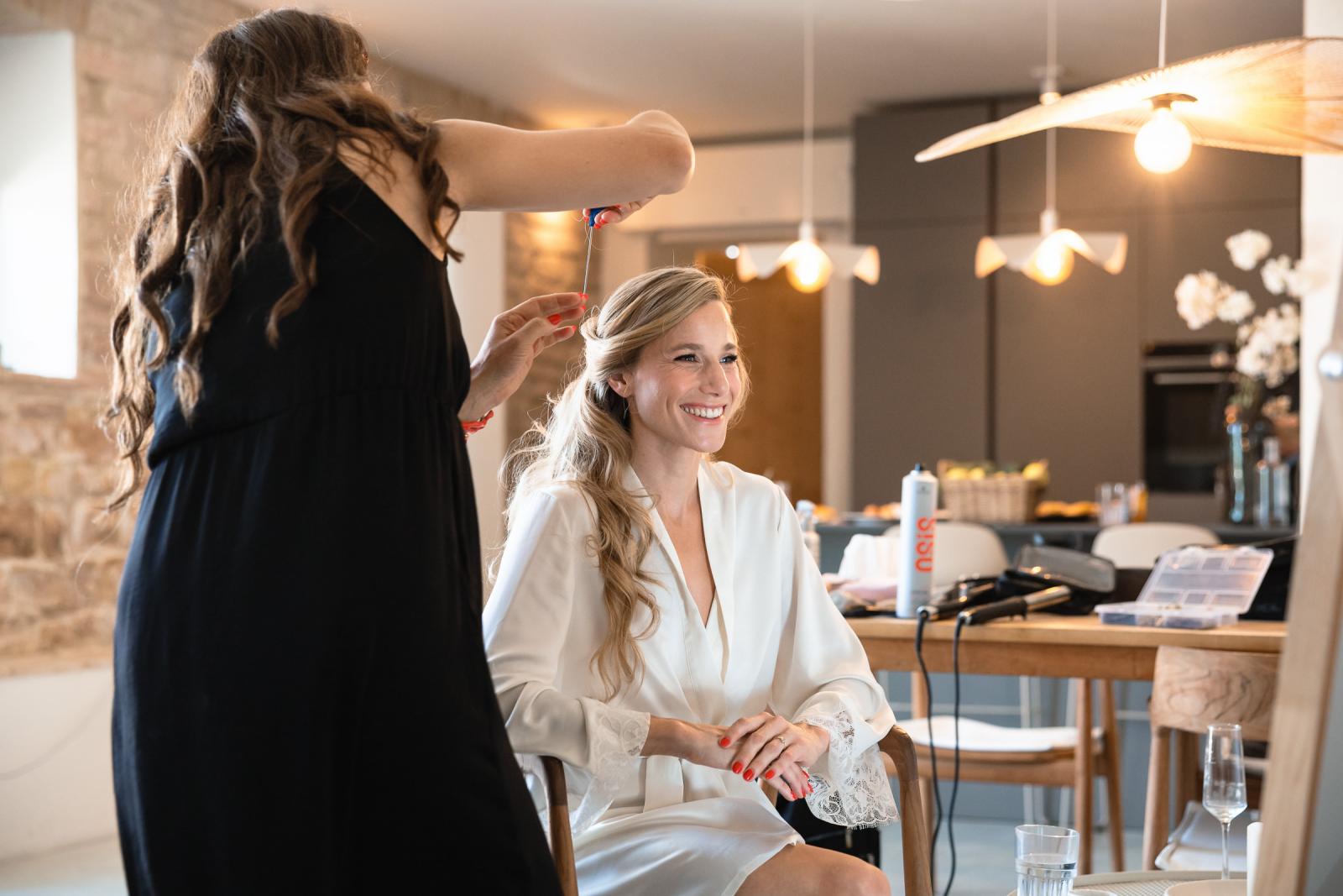 Smiling bride Gemmy sitting in a silk robe during final wedding hair and makeup prep