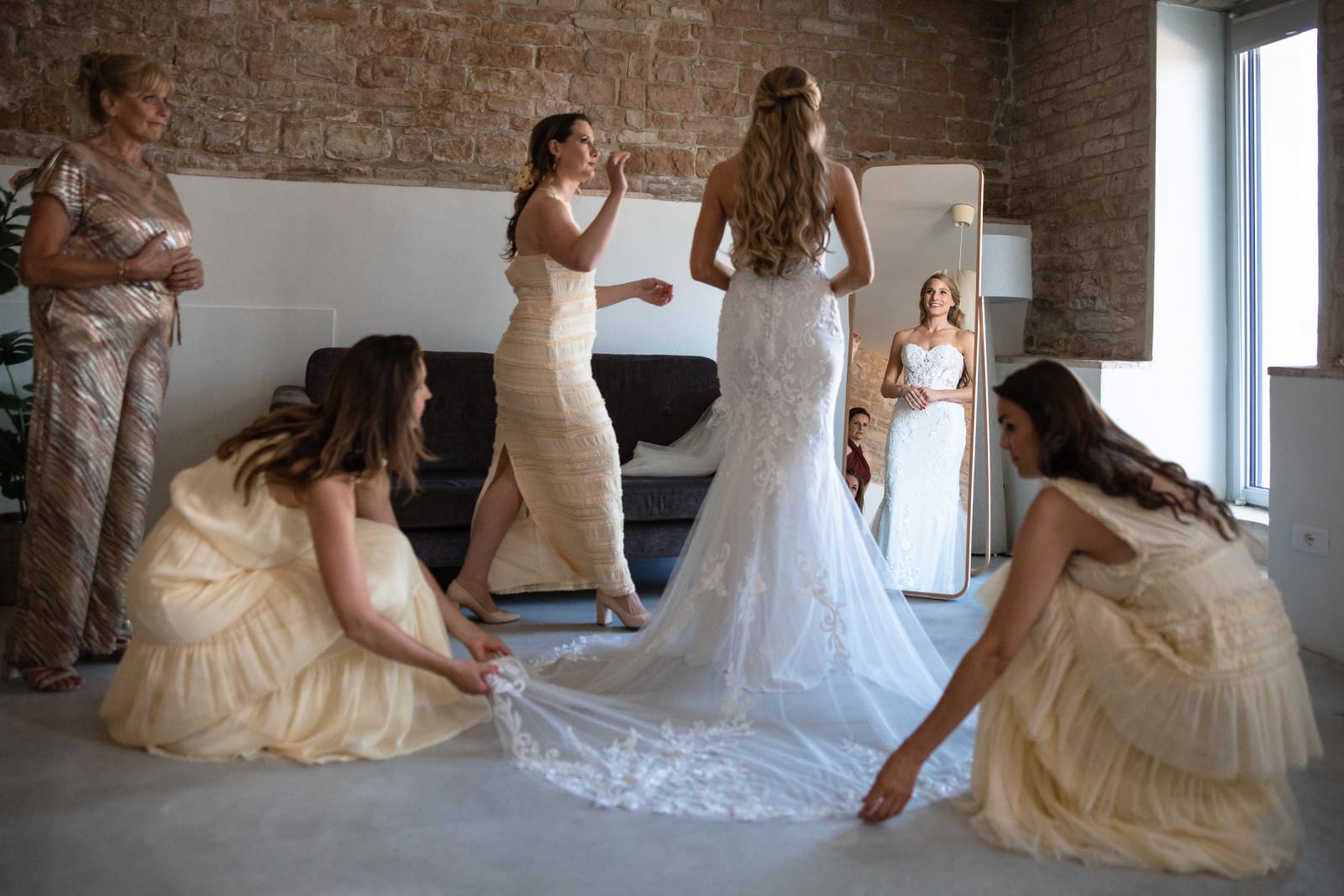 Bride Gemmy checking her complete wedding look in a full-length mirror surrounded by bridesmaids