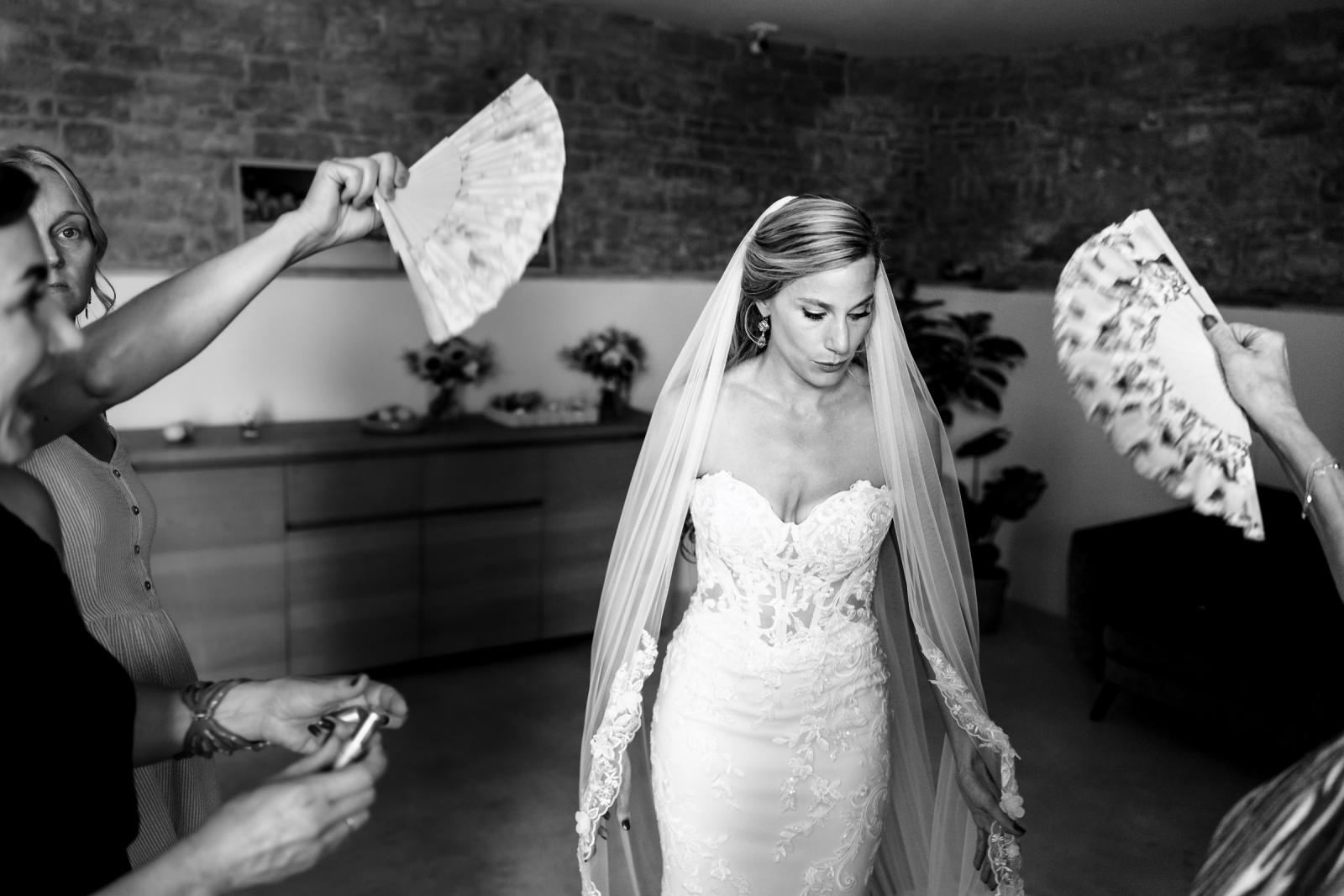 Black and white shot of helpers fanning bride Gemmy in her lace wedding dress on a warm day