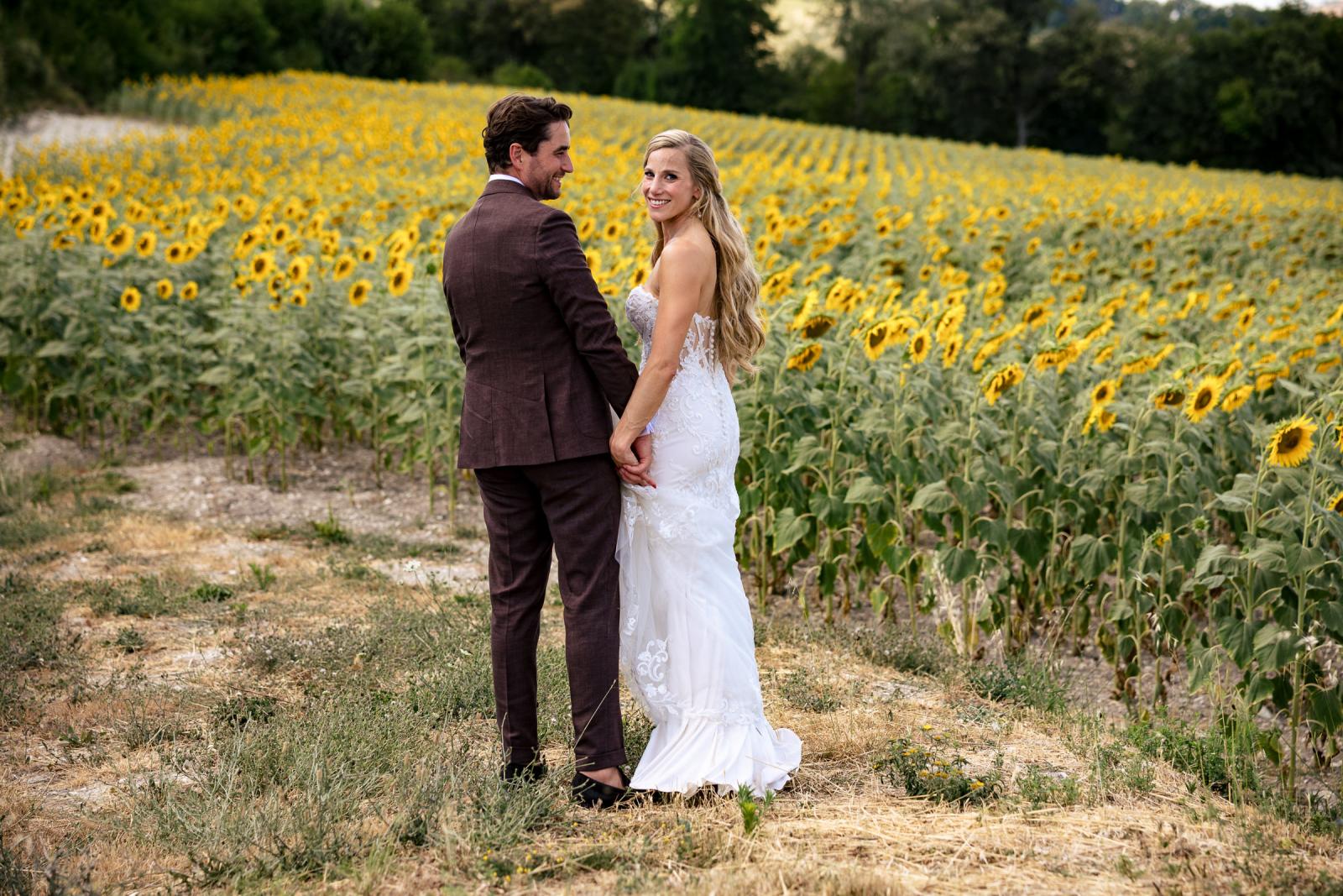 Bride Gemmy turning back to look at camera while holding hands with groom Niels in sunflower field