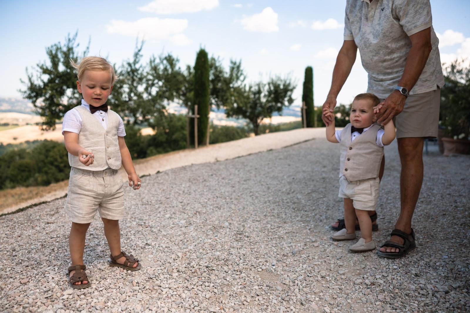 Two young page boys in matching linen waistcoats playing on gravel path at Le Stonghe
