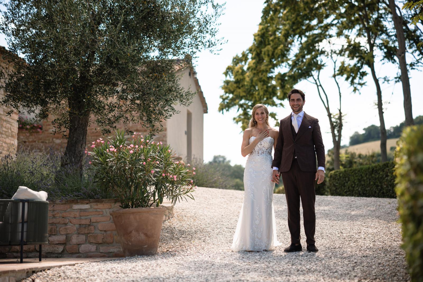 Bride Gemmy and groom Niels holding hands and smiling on gravel path by potted oleander