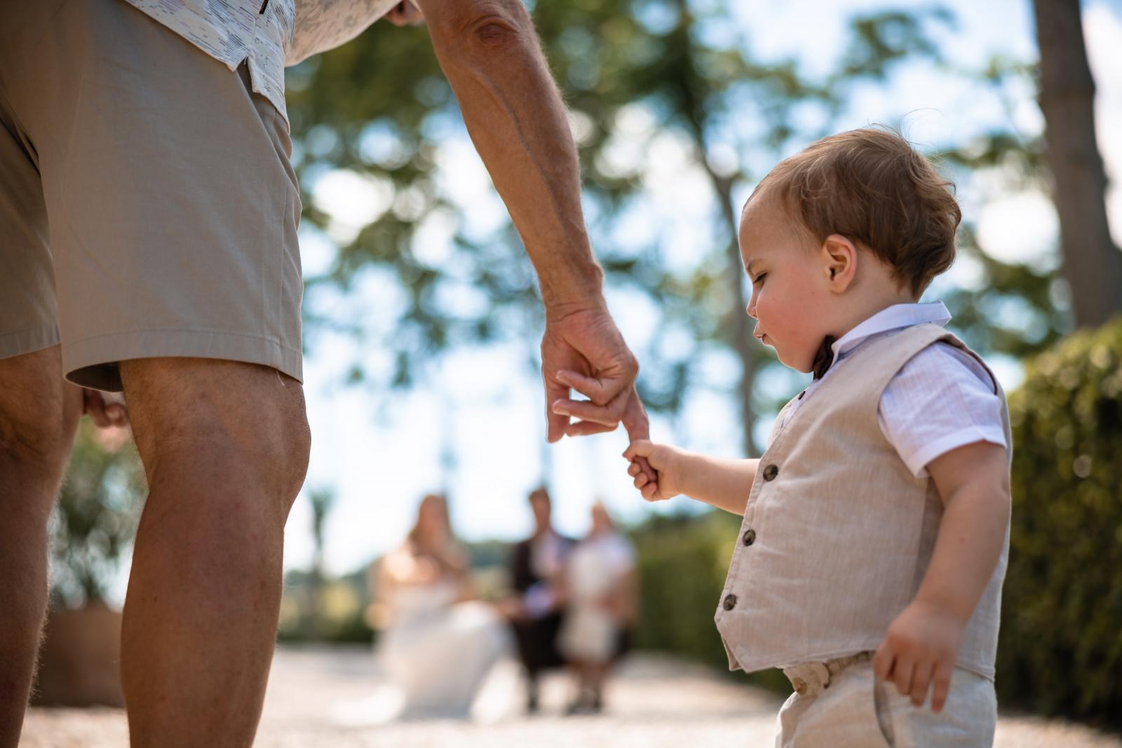 Close-up shot of toddler page boy holding hands with relative on gravel path