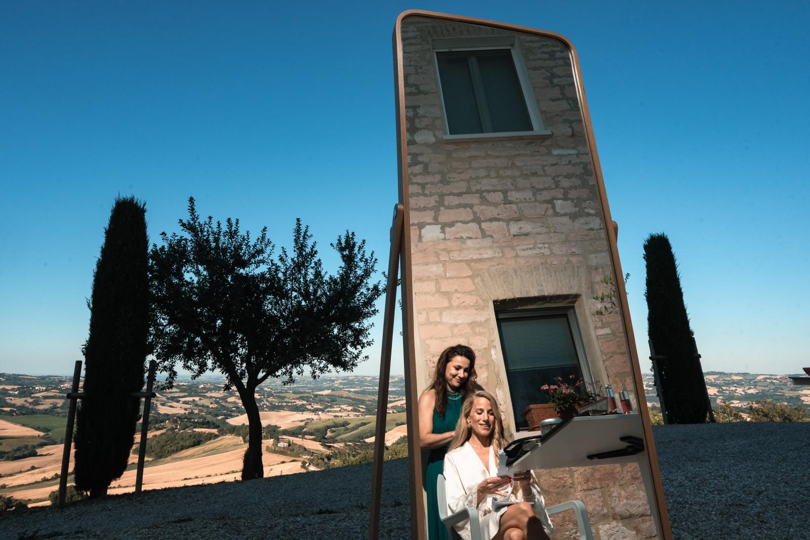Bride getting hair done in front of a mirror with scenic Le Marche countryside background