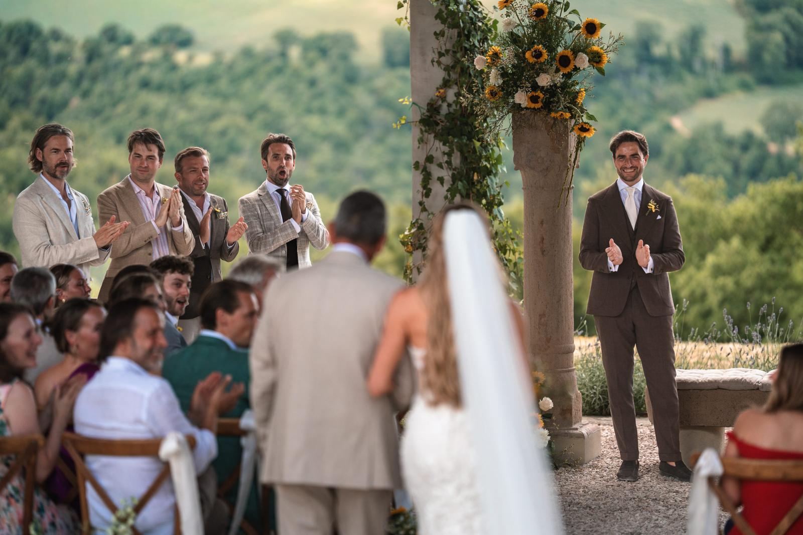 Groom Niels smiling as bride Gemmy walks down aisle escorted by father at wedding