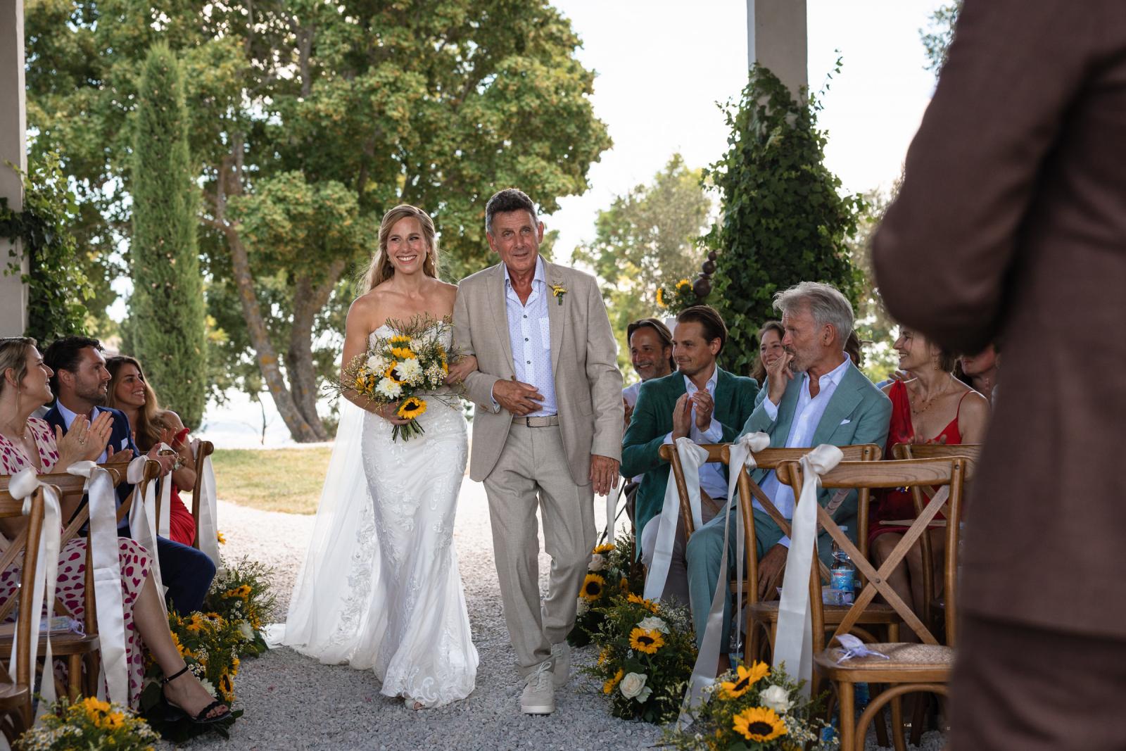 Bride Gemmy smiling in wedding gown walking down aisle with father at Le Stonghe
