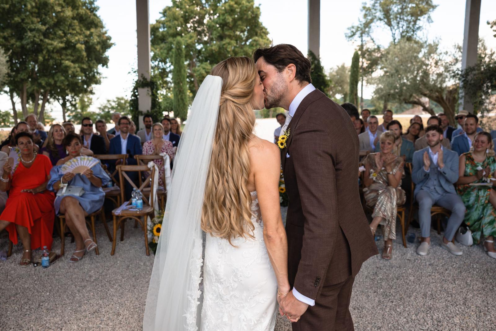 Bride Gemmy and groom Niels kissing at aisle entrance surrounded by wedding guests