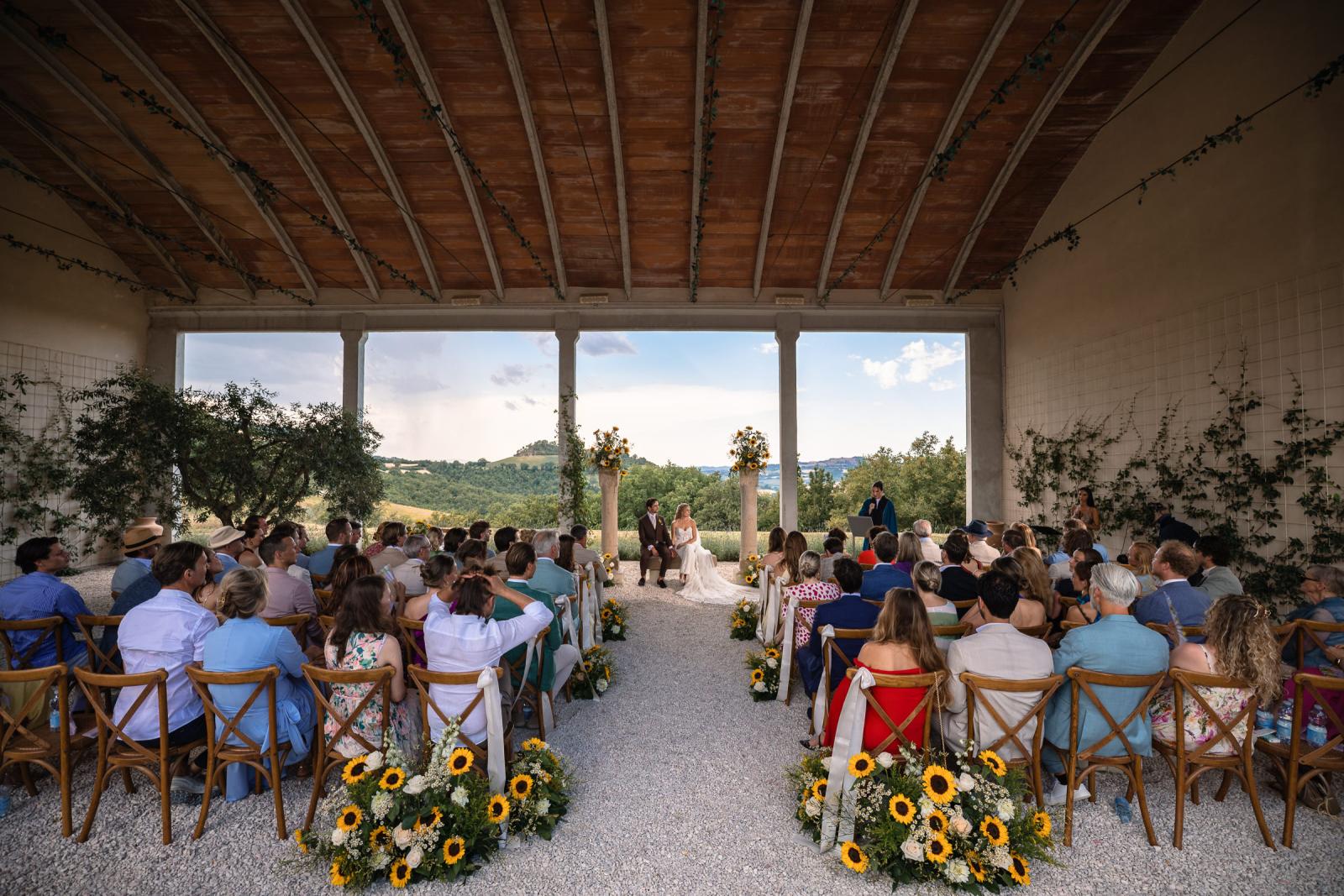 Wide view of Italian covered terrace wedding ceremony with sunflower floral arrangements