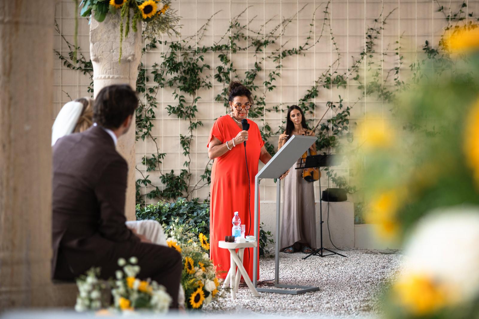 Mother giving speech at podium during ceremony with violinist in background