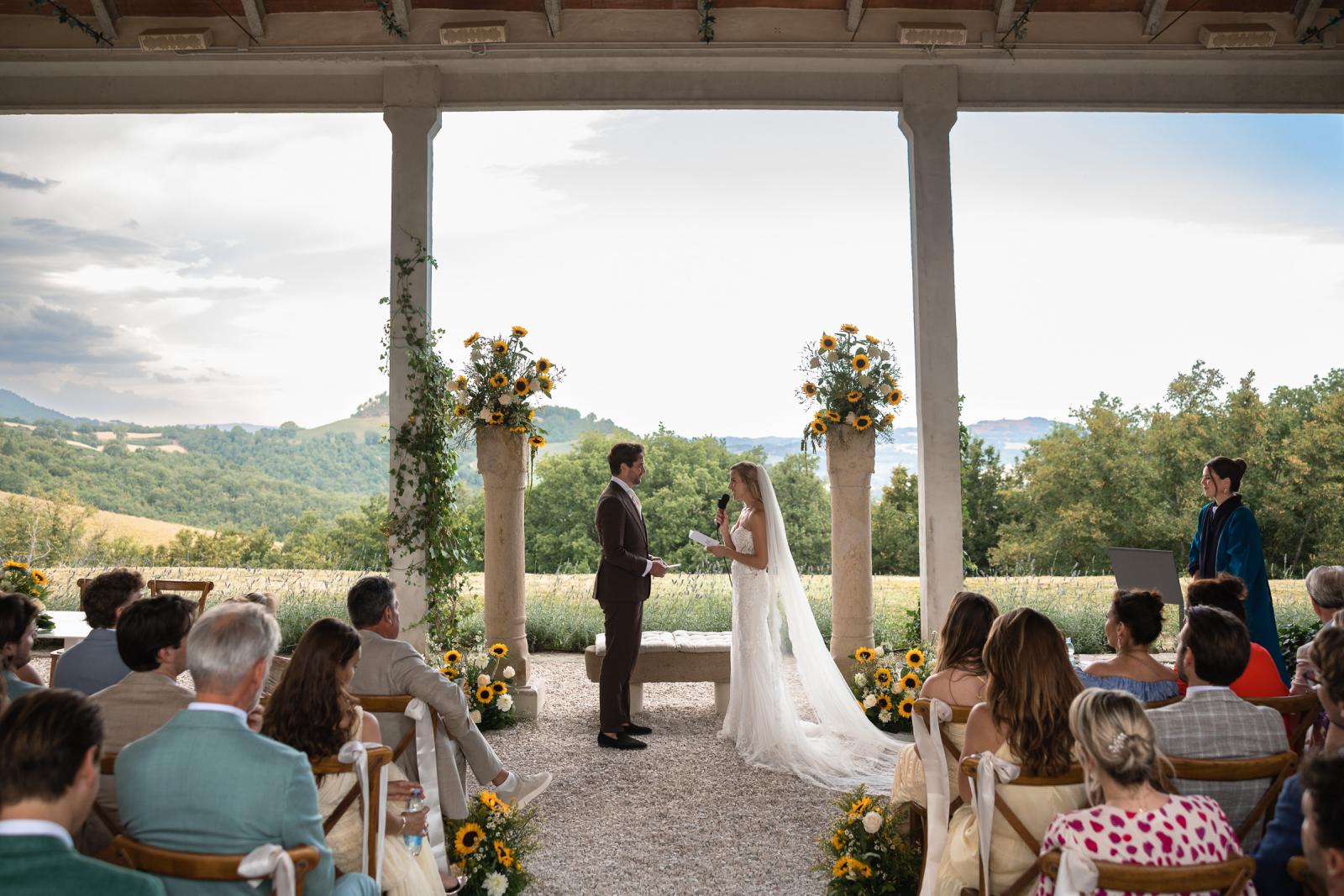 Bride Gemmy reading vows to groom Niels under covered terrace overlooking Italian hills