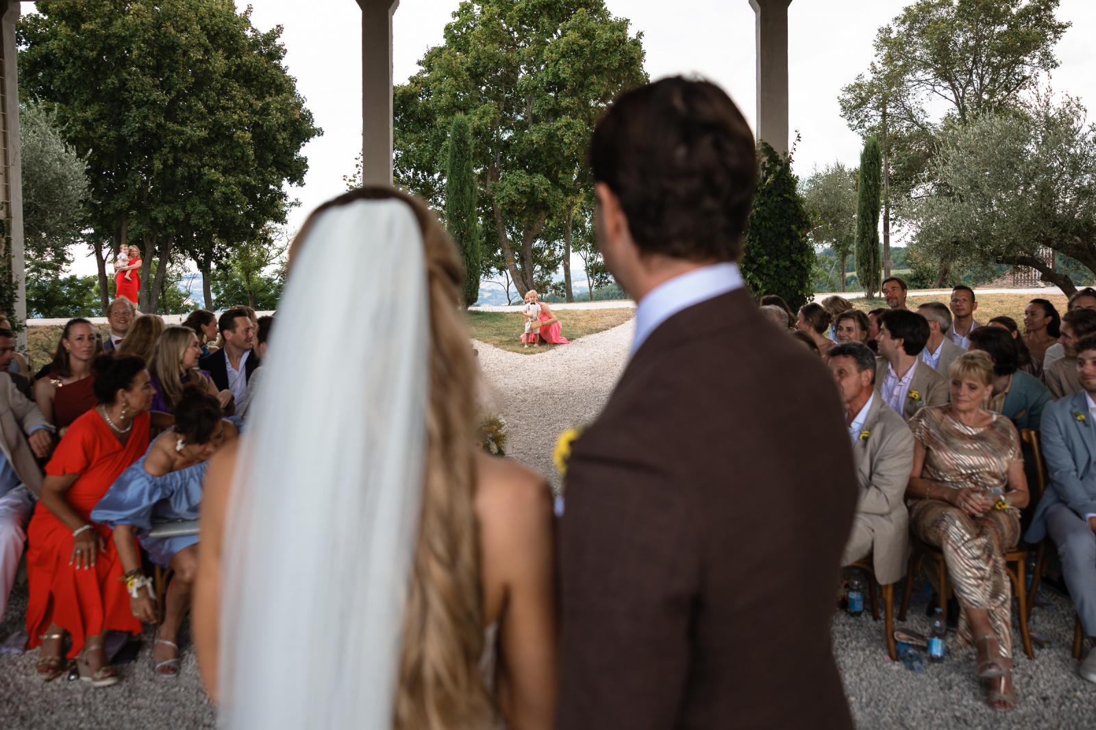 Over the shoulder view of bride and groom watching toddler during wedding ceremony