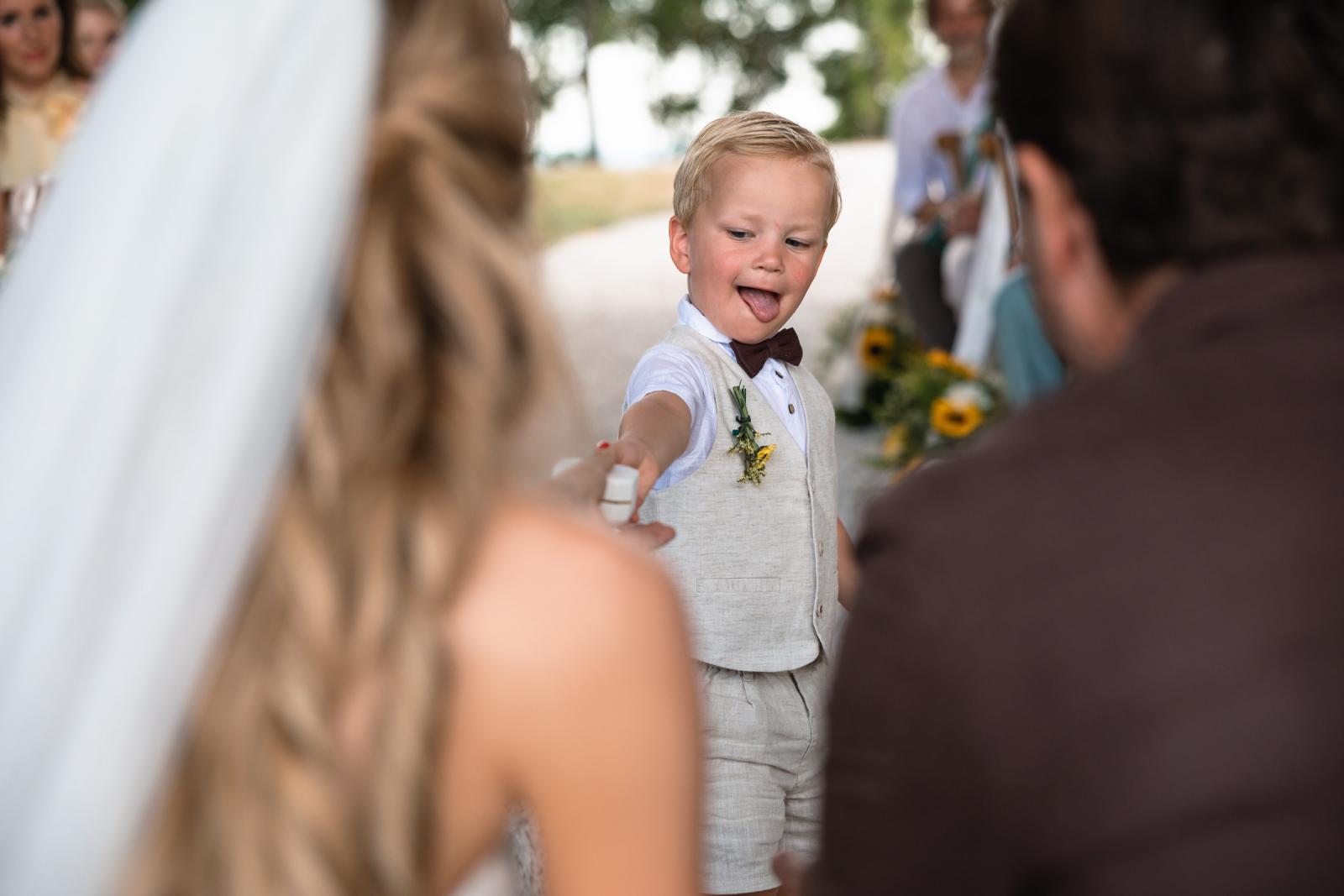 Young ring bearer handing wedding rings to bride and groom during ceremony