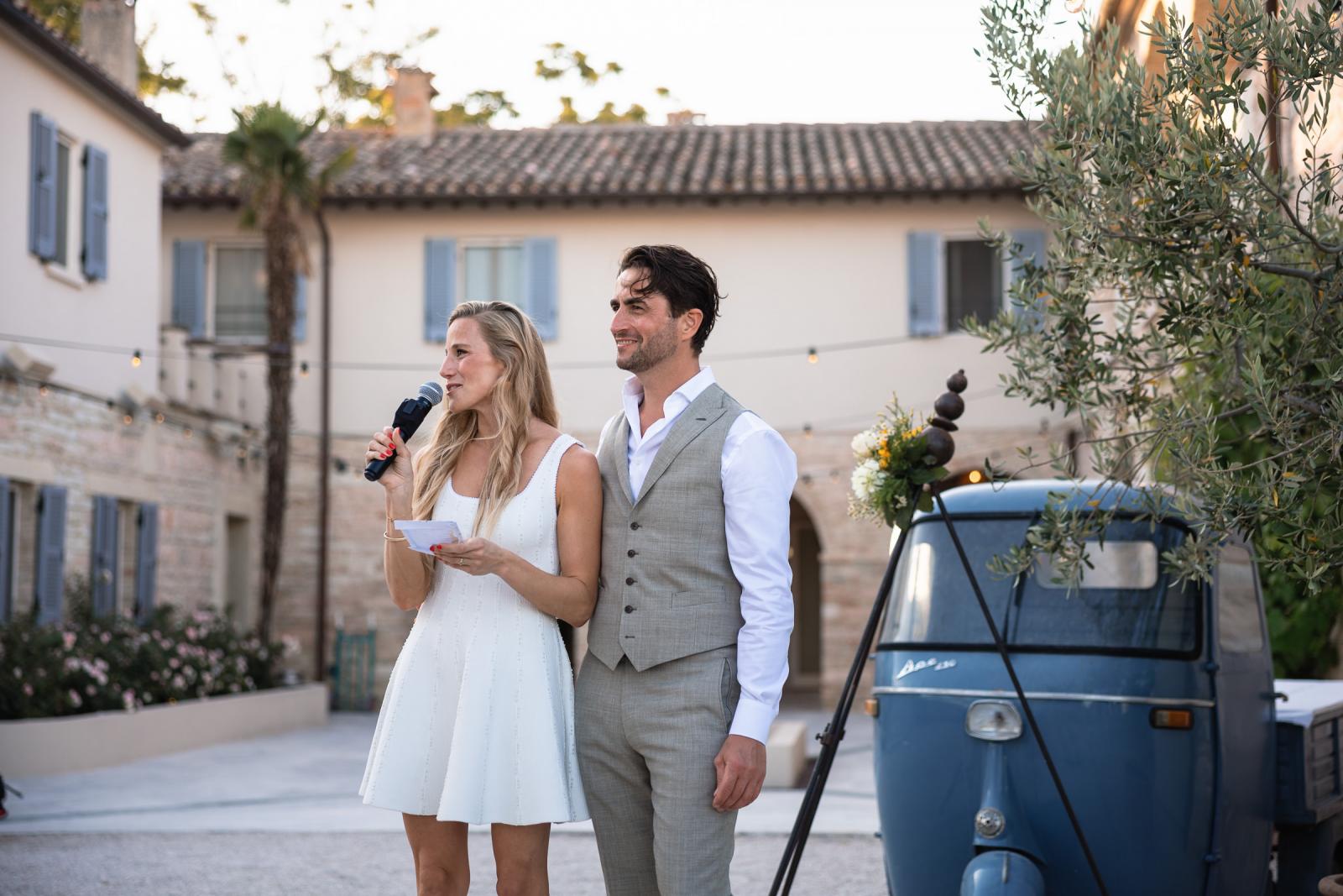 Bride Gemmy and groom Niels giving a welcome speech next to a classic blue Piaggio Ape
