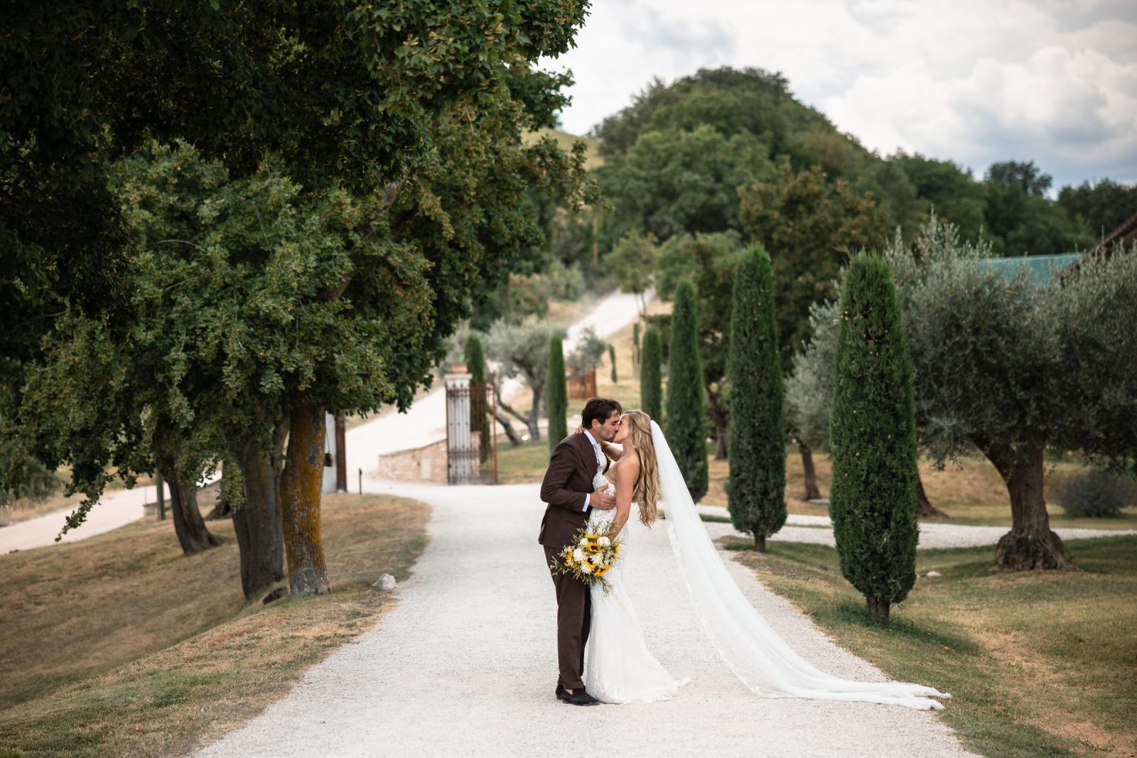 Groom Niels dipping bride Gemmy for a kiss on tree-lined gravel path at Le Stonghe