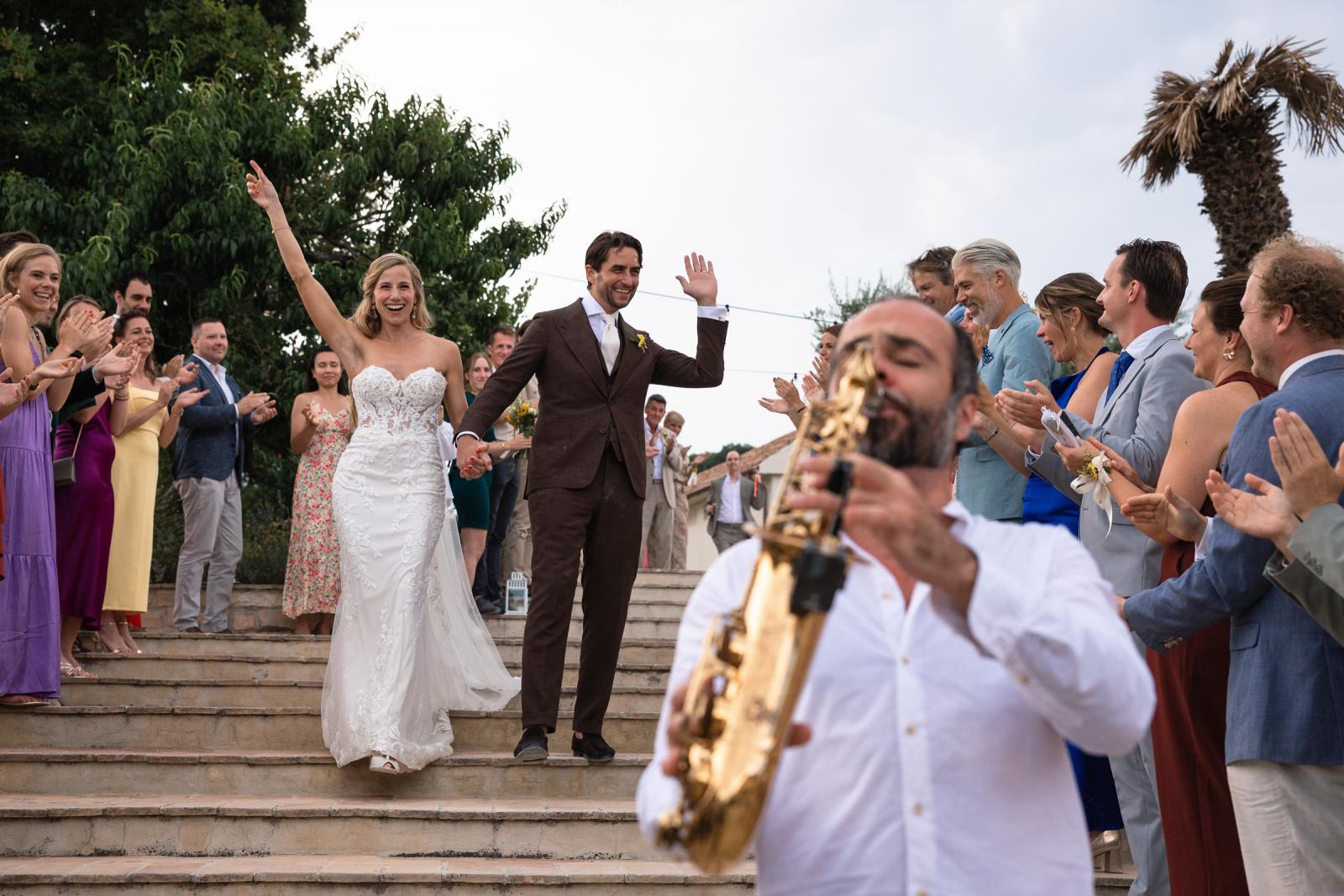 Bride Gemmy and groom Niels walking down stairs cheered by wedding guests with live saxophonist