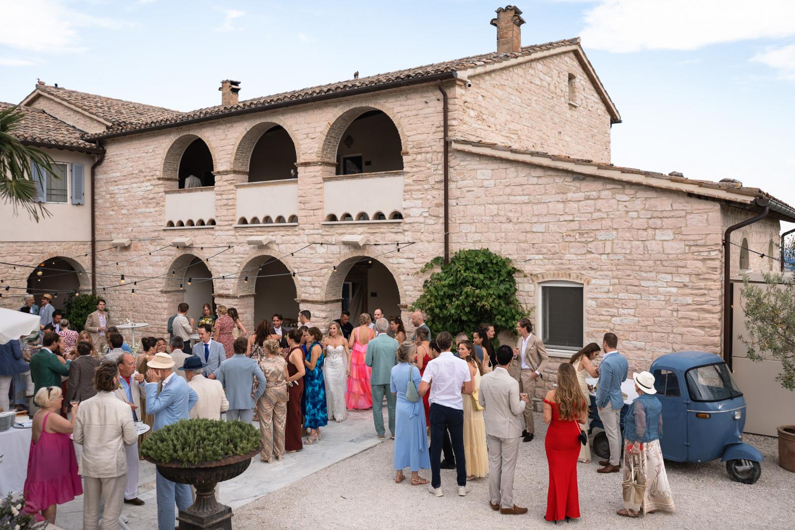 Wide outdoor shot of wedding guests gathered in courtyard of Italian stone villa Le Stonghe
