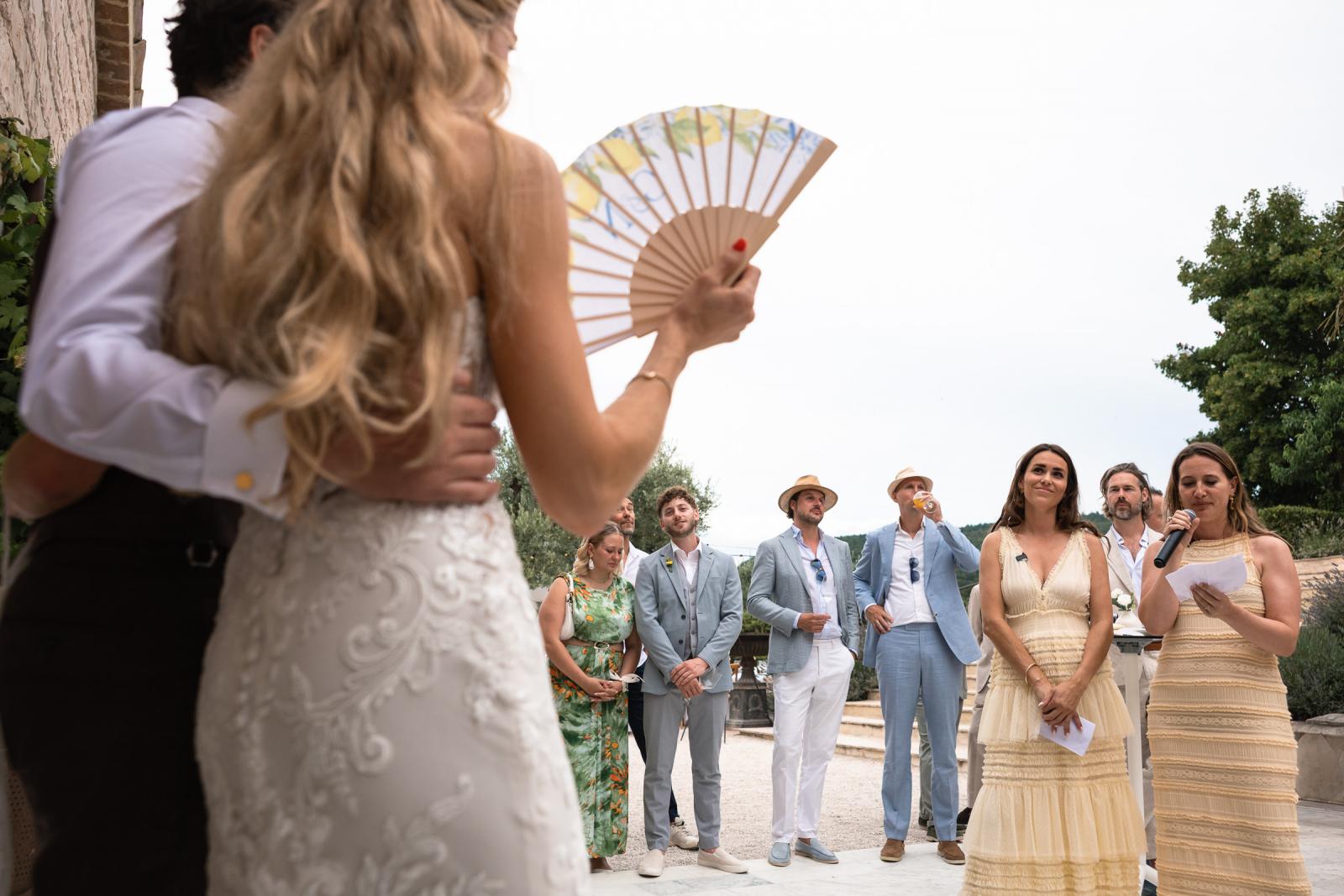 Bride Gemmy holding paper fan while guests give speeches at Italian wedding reception
