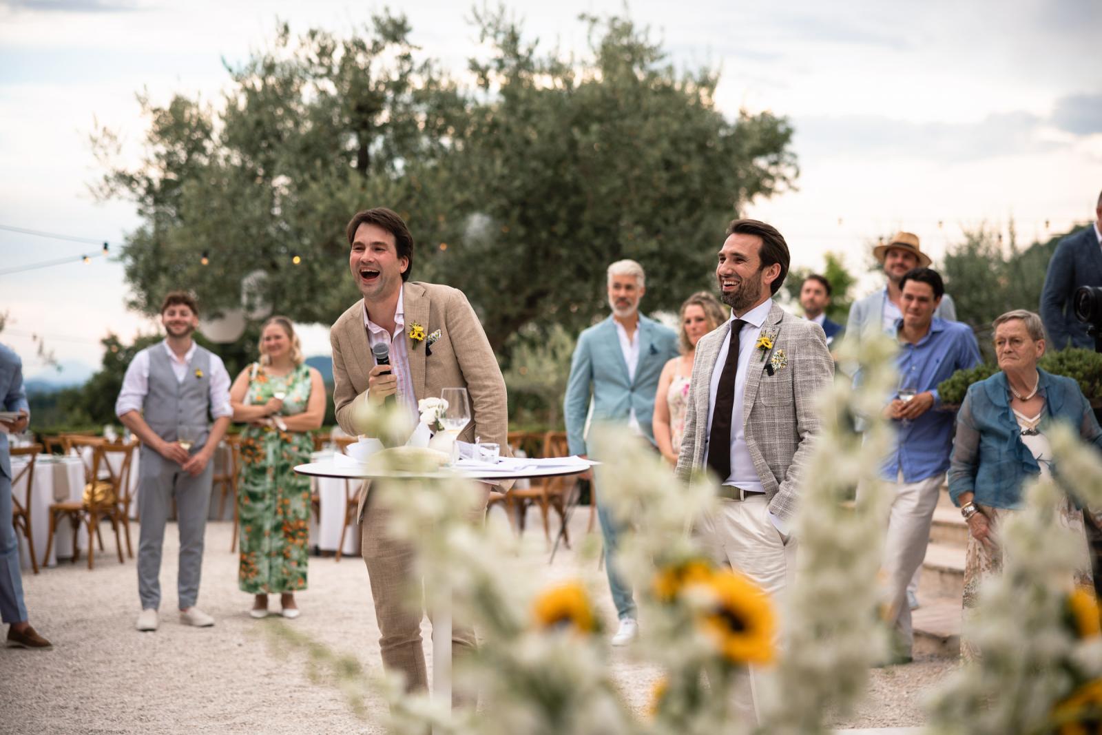 Groomsman giving humorous speech into microphone at outdoor wedding at Le Stonghe