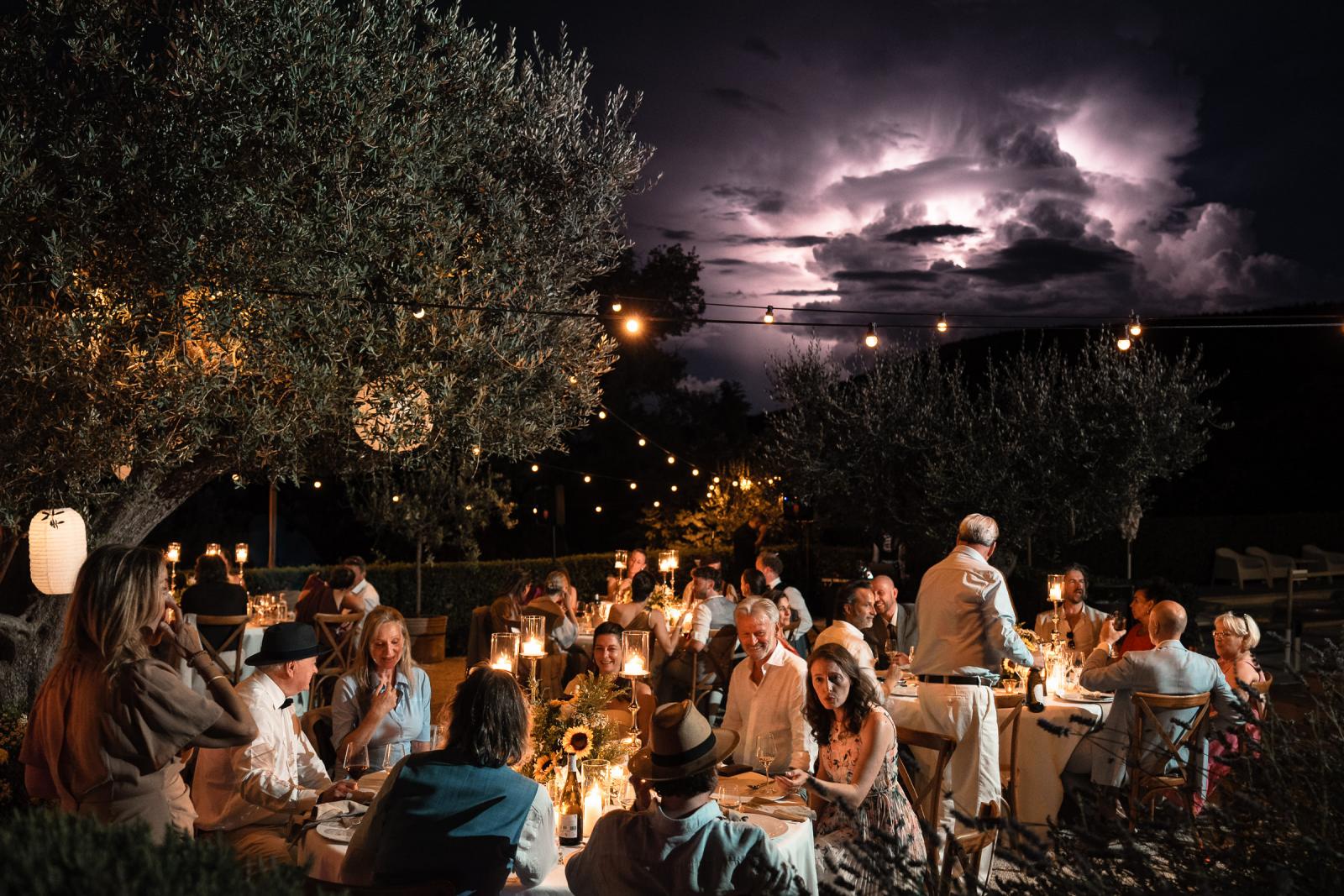 Wedding guests dining at night outdoors at Le Stonghe with lightning storm in background sky