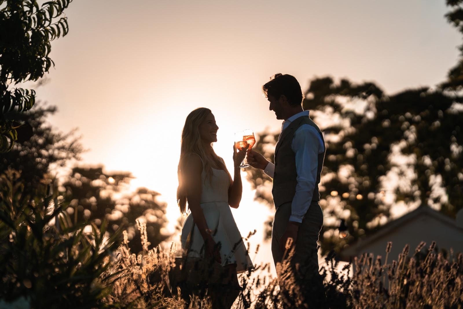 Silhouette of bride and groom toasting Spritz cocktails in lavender field during sunset