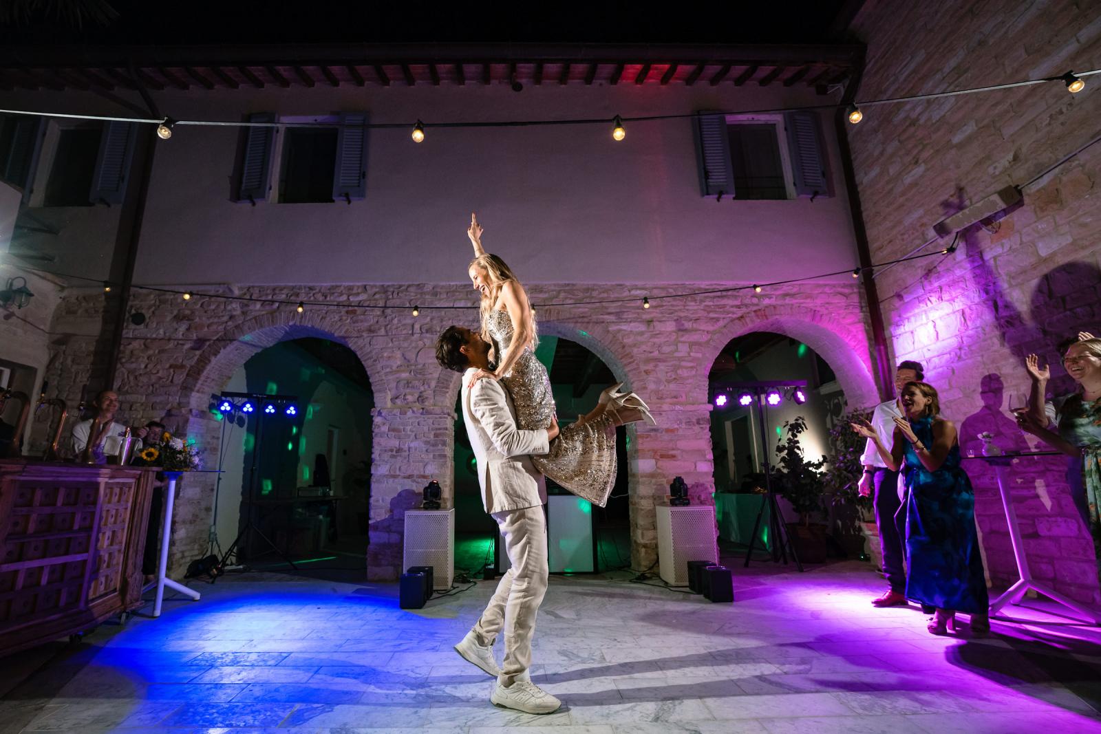 Groom Niels lifting bride Gemmy during energetic first dance under party lighting in courtyard