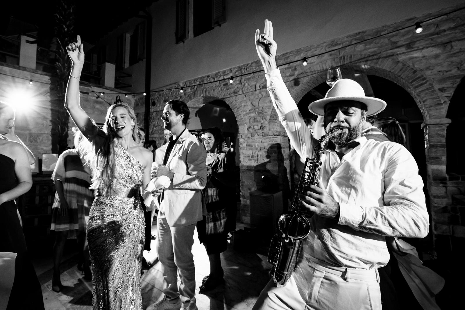Black and white shot of saxophone player in fedora hat playing beside bride Gemmy dancing