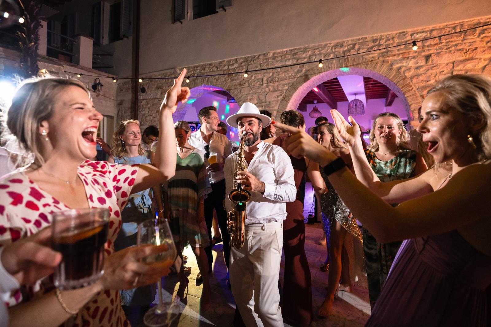 Saxophone player in white fedora hat playing for cheering bride Gemmy and party guests