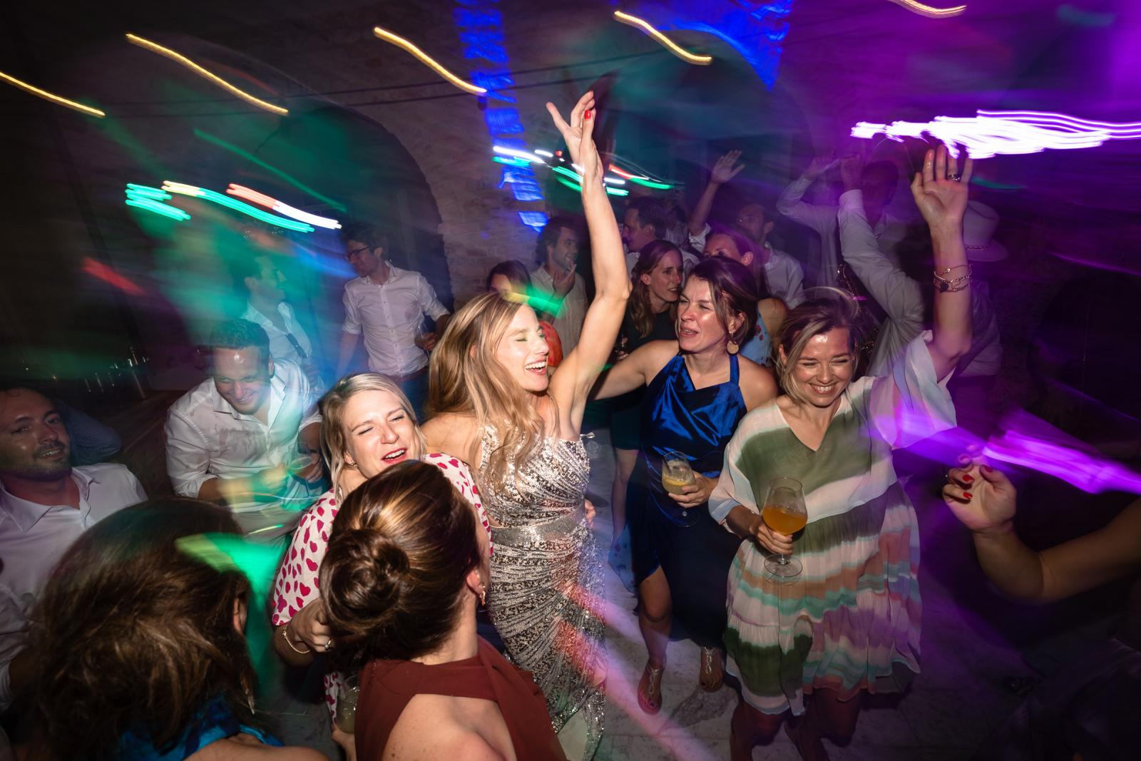 Dynamic wide shot of bride Gemmy dancing with arm raised in middle of crowded dance floor
