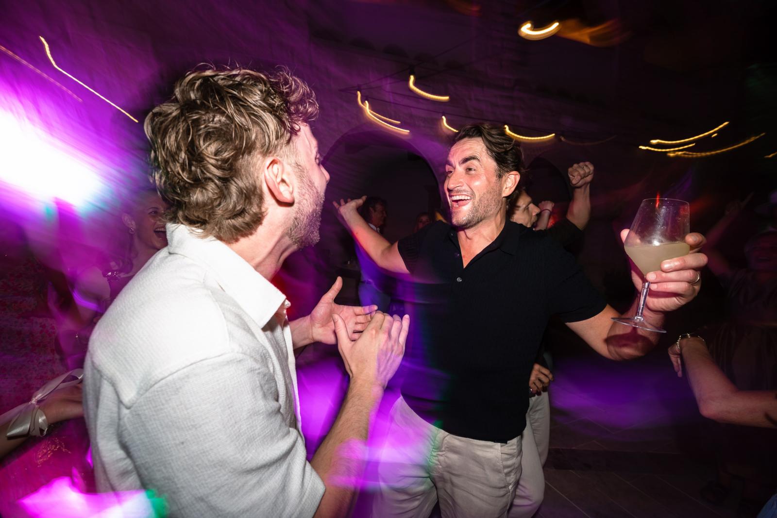Groom Niels laughing and dancing with guest under vibrant purple party lighting