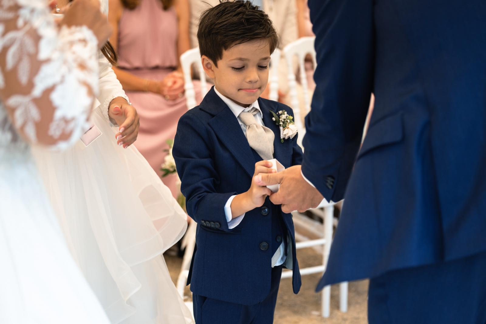 Het zoontje van George en Iris overhandigt geconcentreerd de trouwringen aan zijn vader tijdens de ceremonie.