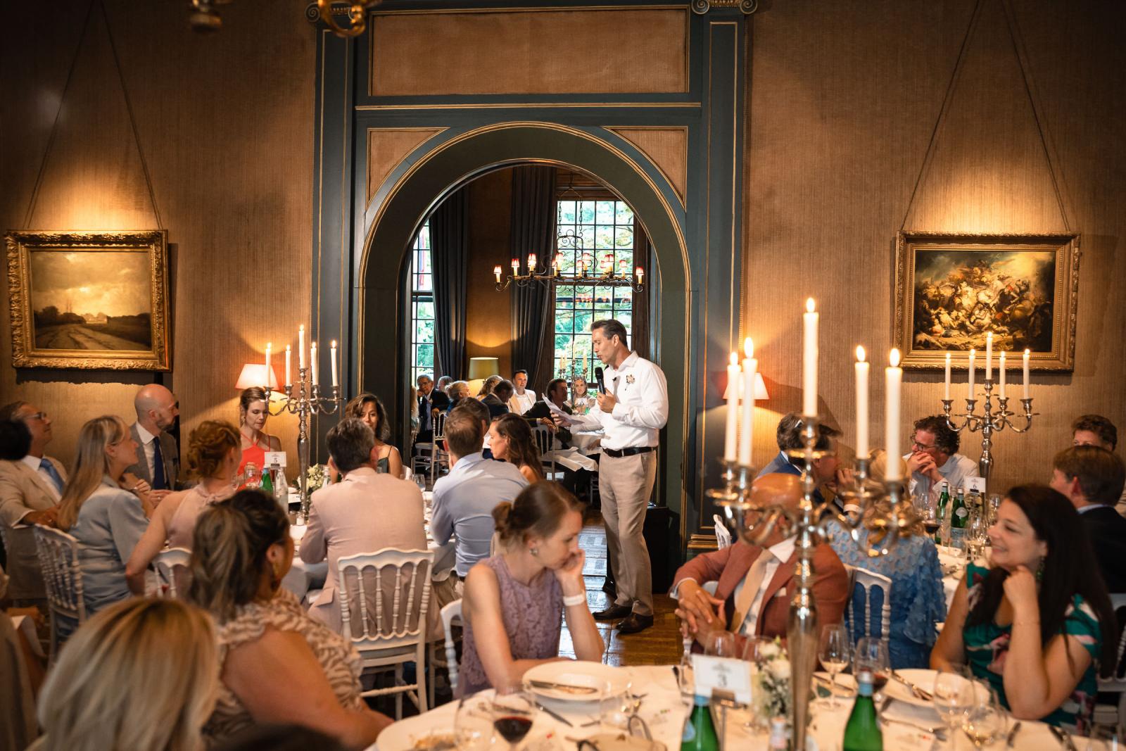 Sfeervol overzicht van het bruidsdiner bij kaarslicht in de statige eetzaal van Kasteel de Wittenburg terwijl er een speech wordt gehouden.