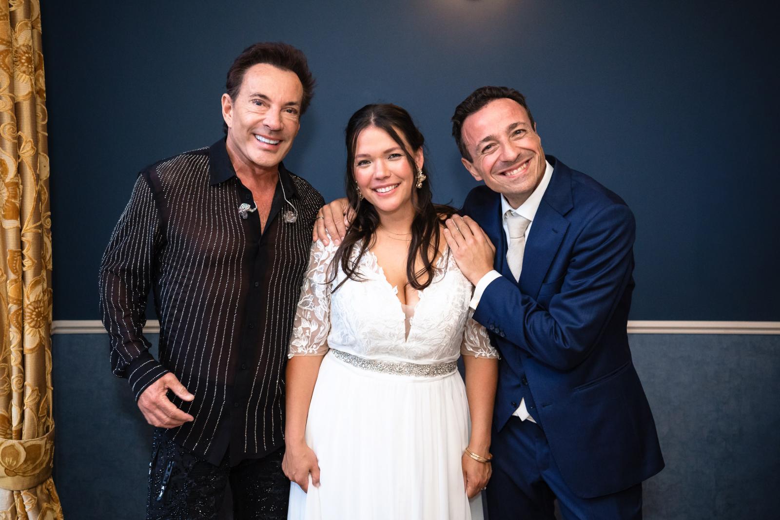 Verrassingsact Gerard Joling poseert lachend tussen bruid Iris en bruidegom George vlak voor het optreden.