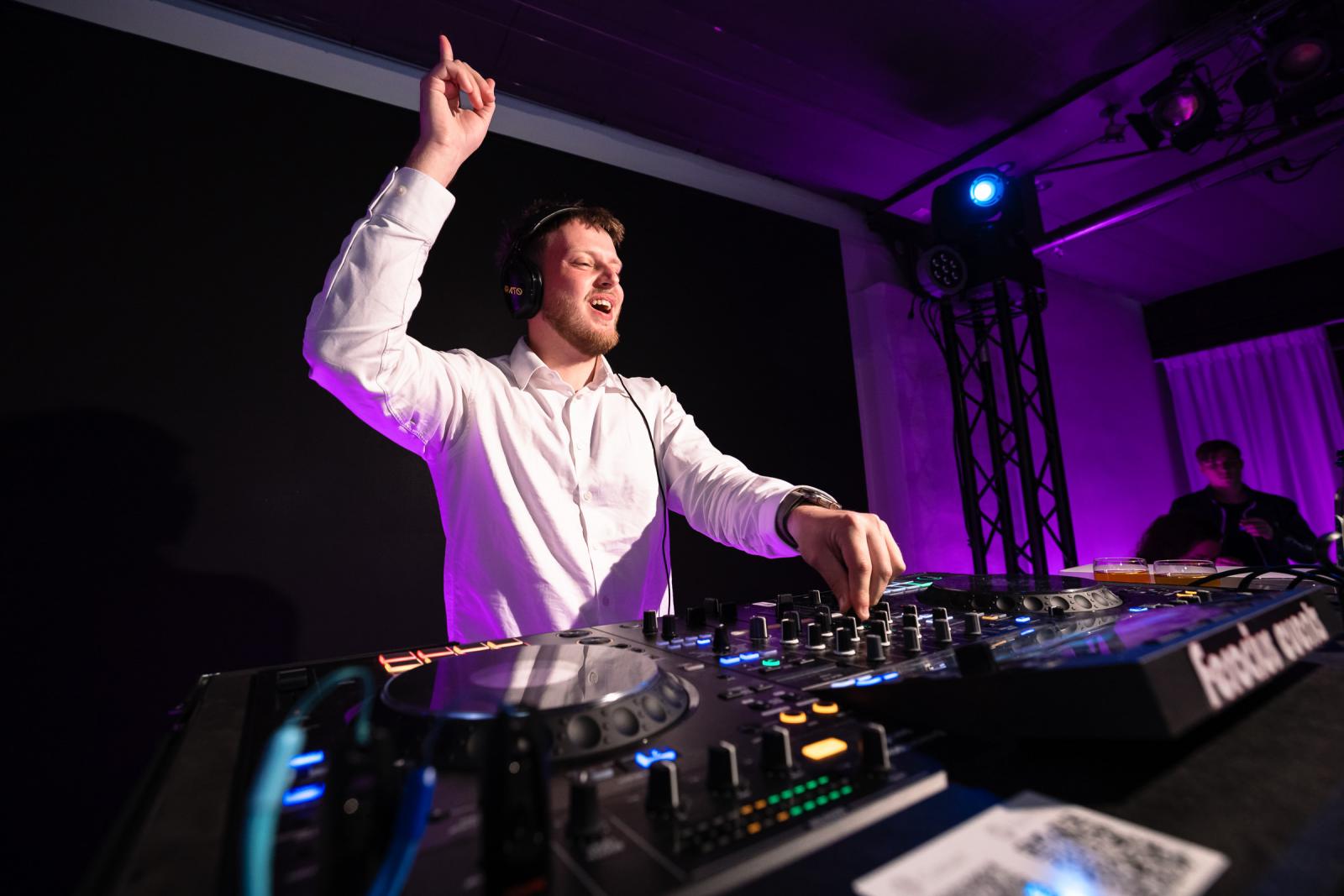 Enthousiaste bruiloft DJ die met één hand in de lucht de sfeer erin brengt achter de DJ-booth.