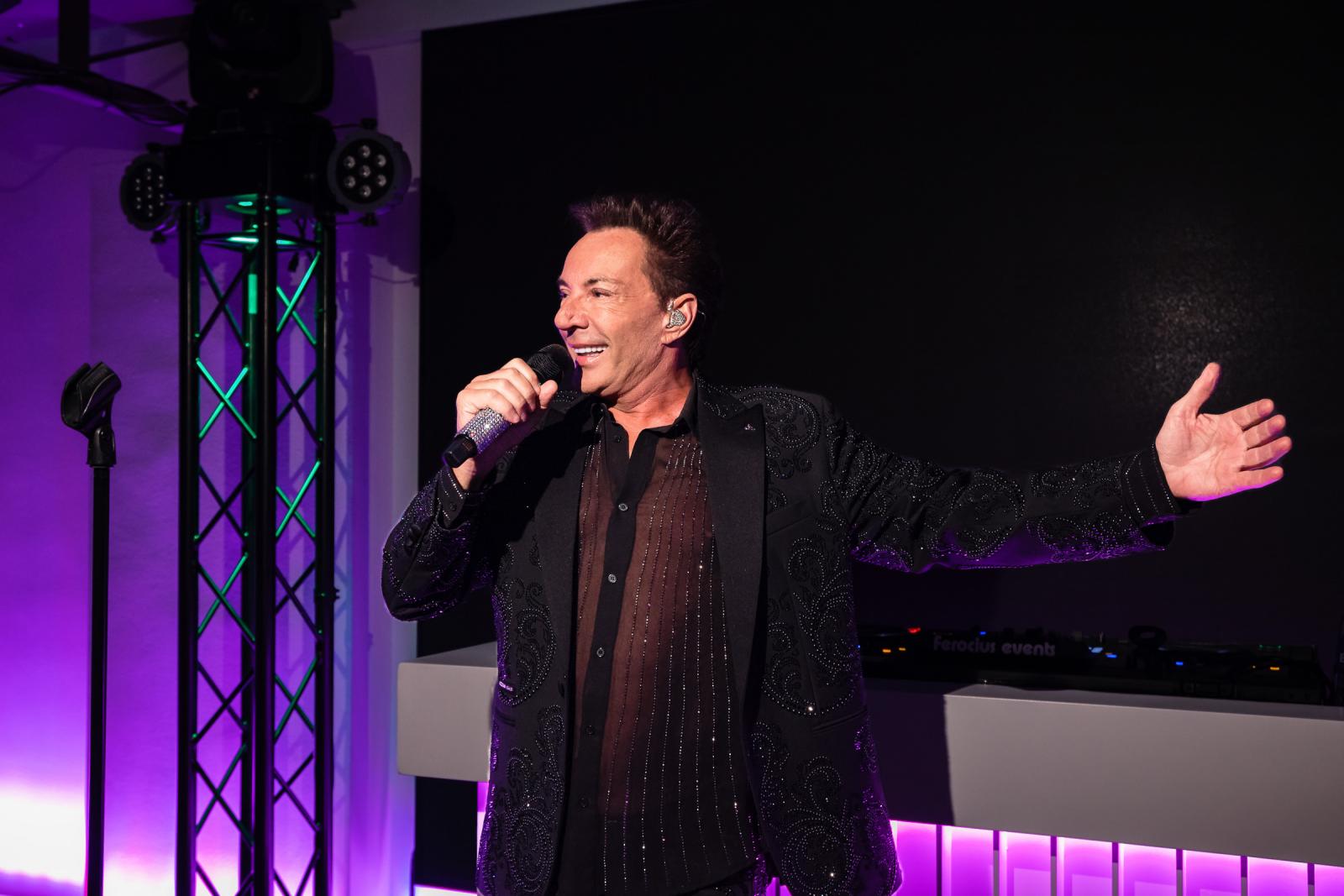 Verrassingsoptreden van Gerard Joling in een glitterjasje met microfoon op het podium tijdens de feestavond van de bruiloft.