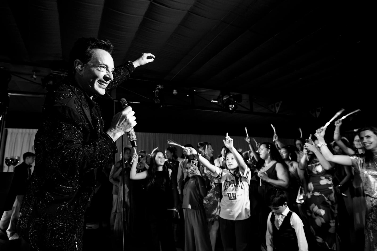 Zwart-wit opname van Gerard Joling die energiek zingt en zwaait naar de zingende gasten op de dansvloer.
