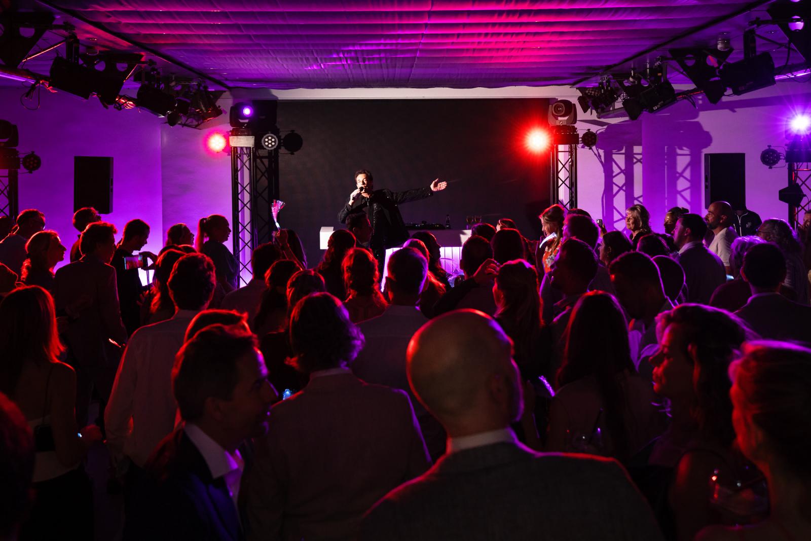Aanzicht van de volle, paars verlichte feestzaal in Kasteel de Wittenburg waar iedereen meezingt met het verrassingsoptreden.