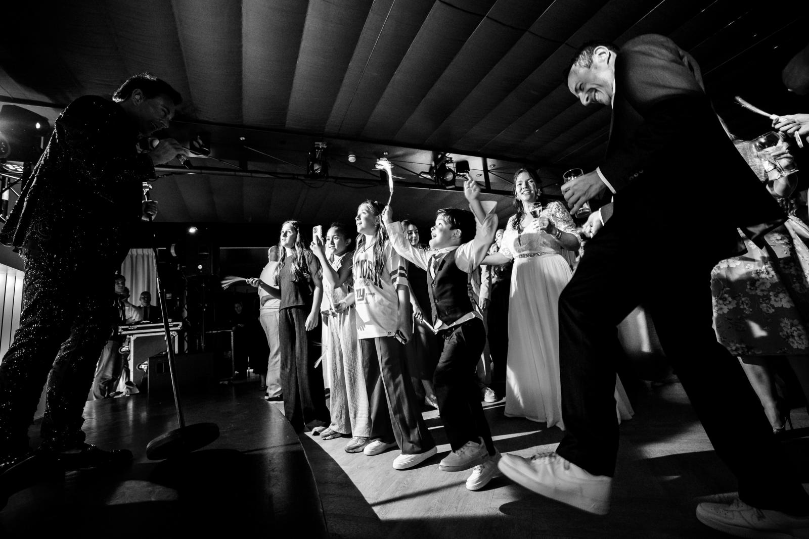 Lage zwart-wit actiefoto van de kinderen die dolenthousiast dansen en springen vlak voor het podium van Gerard Joling.