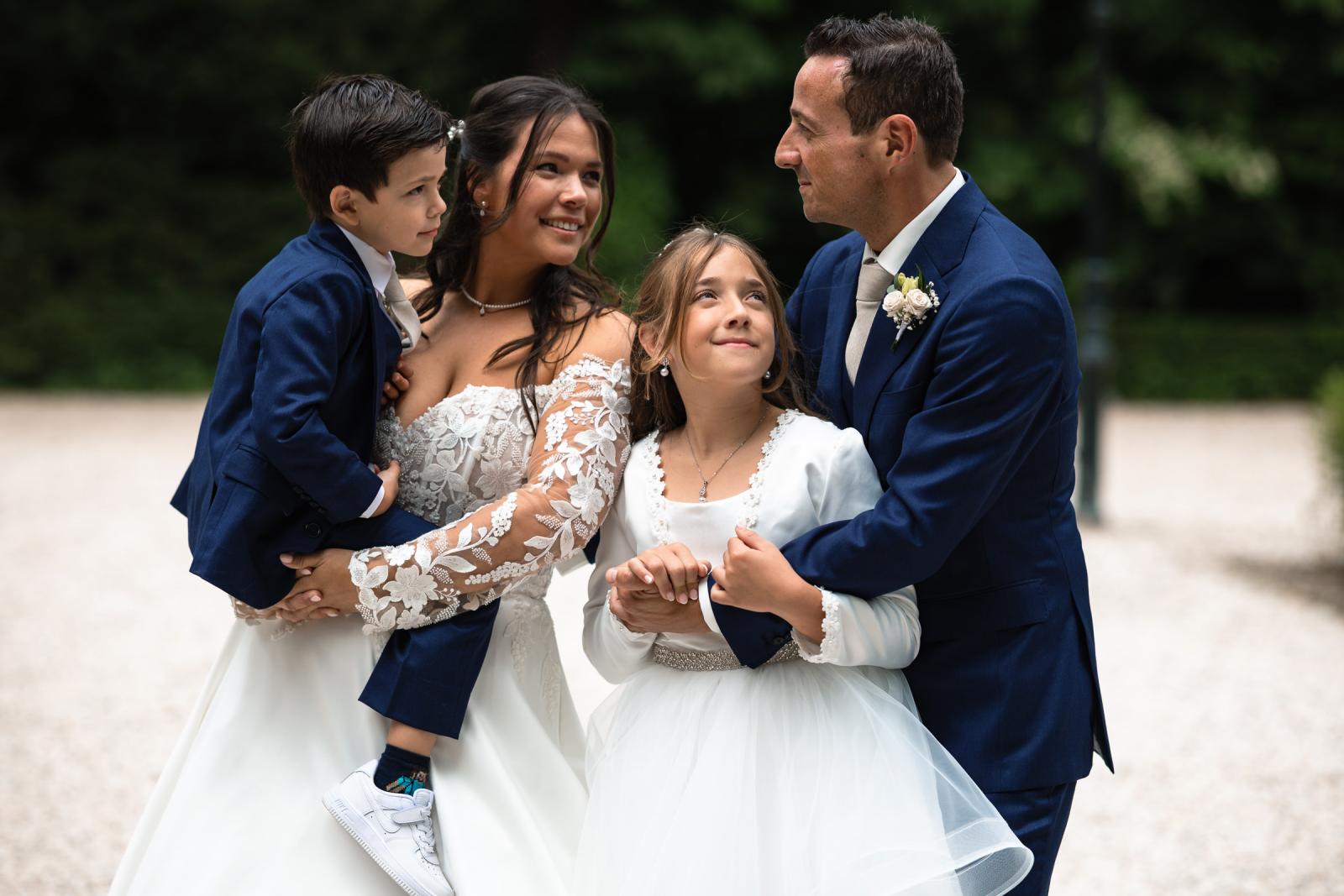 Liefdevol gezinsportret van bruid Iris, bruidegom George en hun twee kinderen in trouwkleding op het landgoed van Kasteel de Wittenburg.