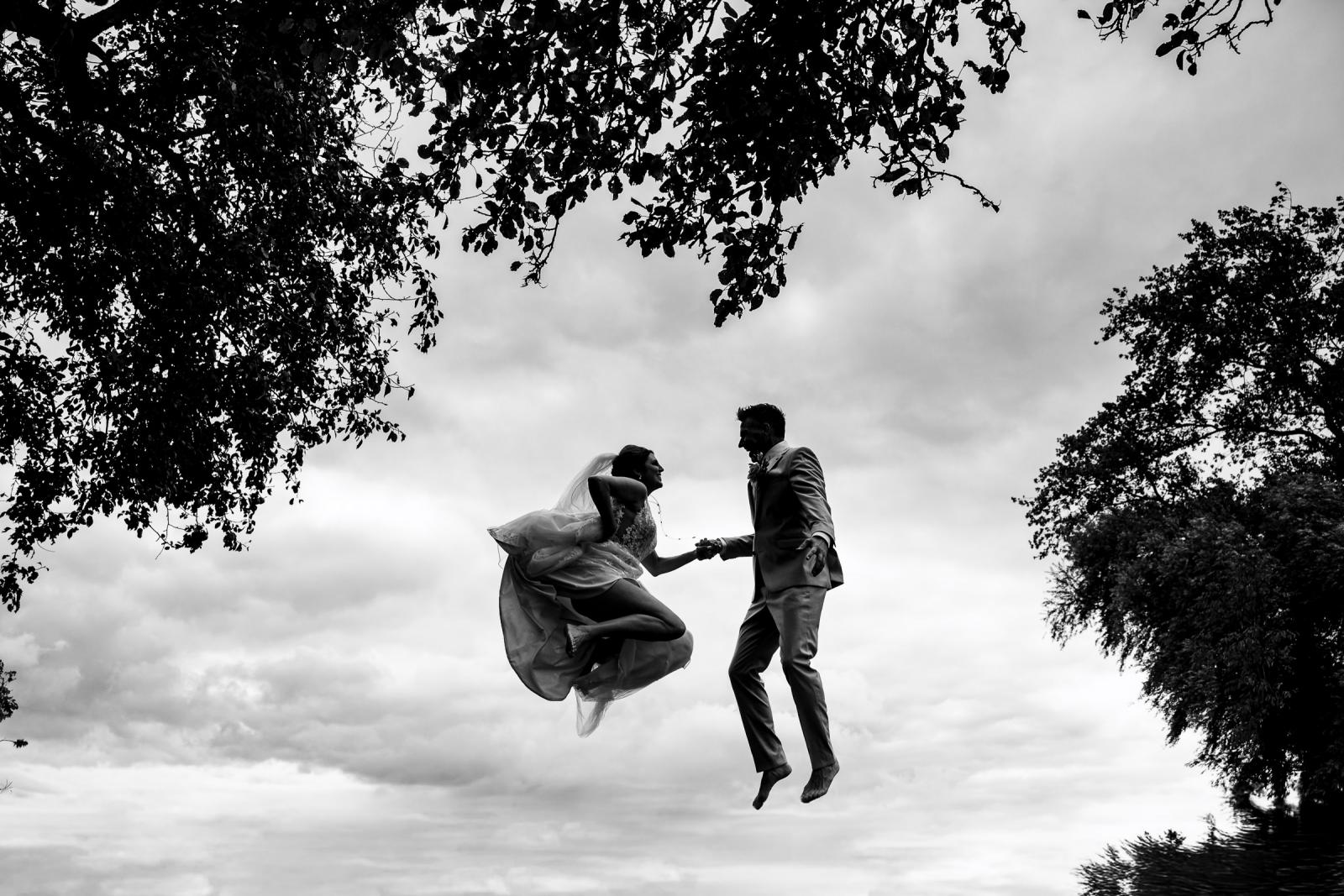 Speels moment: het bruidspaar springt hoog de lucht in op een trampoline, alsof ze in de wolken zweven.